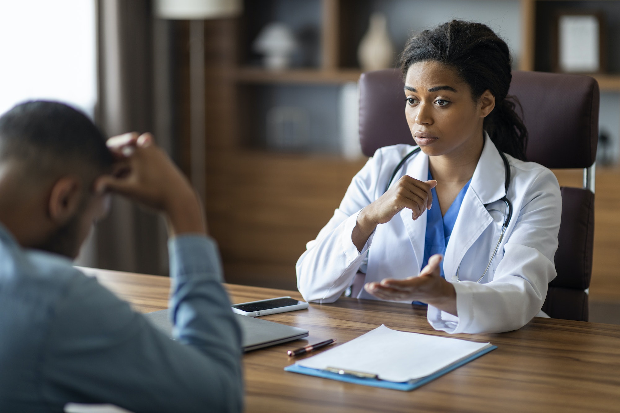 Black woman doctor having conversation with upset sick man patient