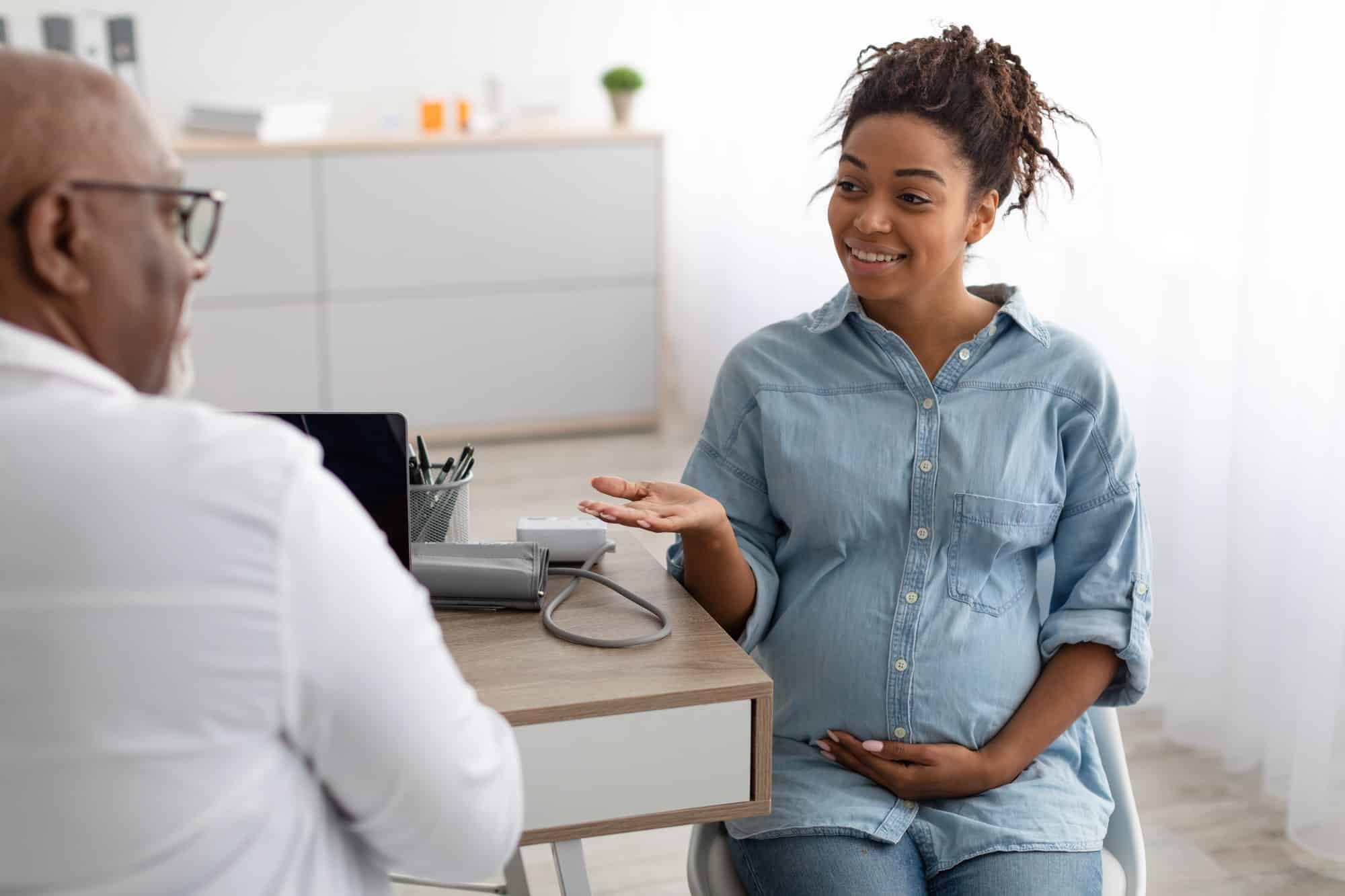 Male doctor consulting young smiling pregnant woman